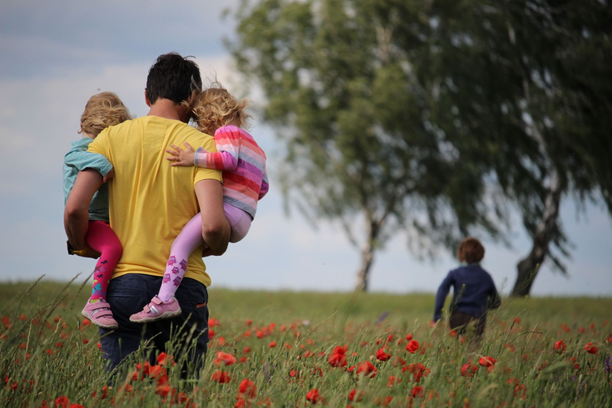 Parent And Children Walking In Field With Flowers