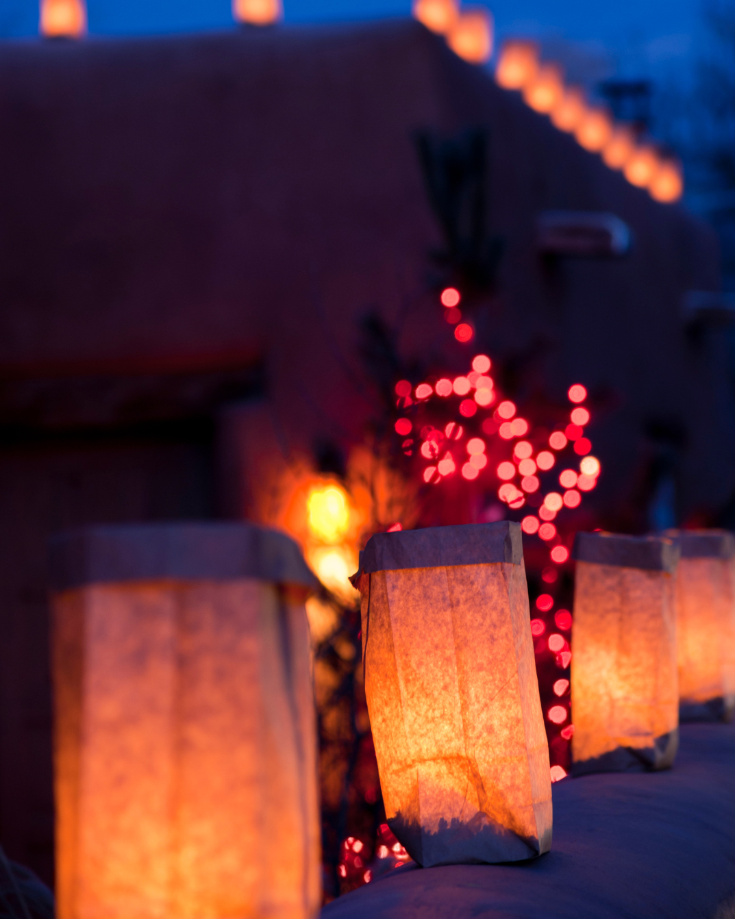 Row Of Luminaria At Night With Twinkling Lights In Background