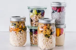 Six glass jars with food prep like rice salads, chia seed pudding and oats