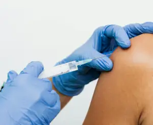 A Person Receives A Vaccination In The Arm, With A Needle Being Inserted By A Gloved Hand.